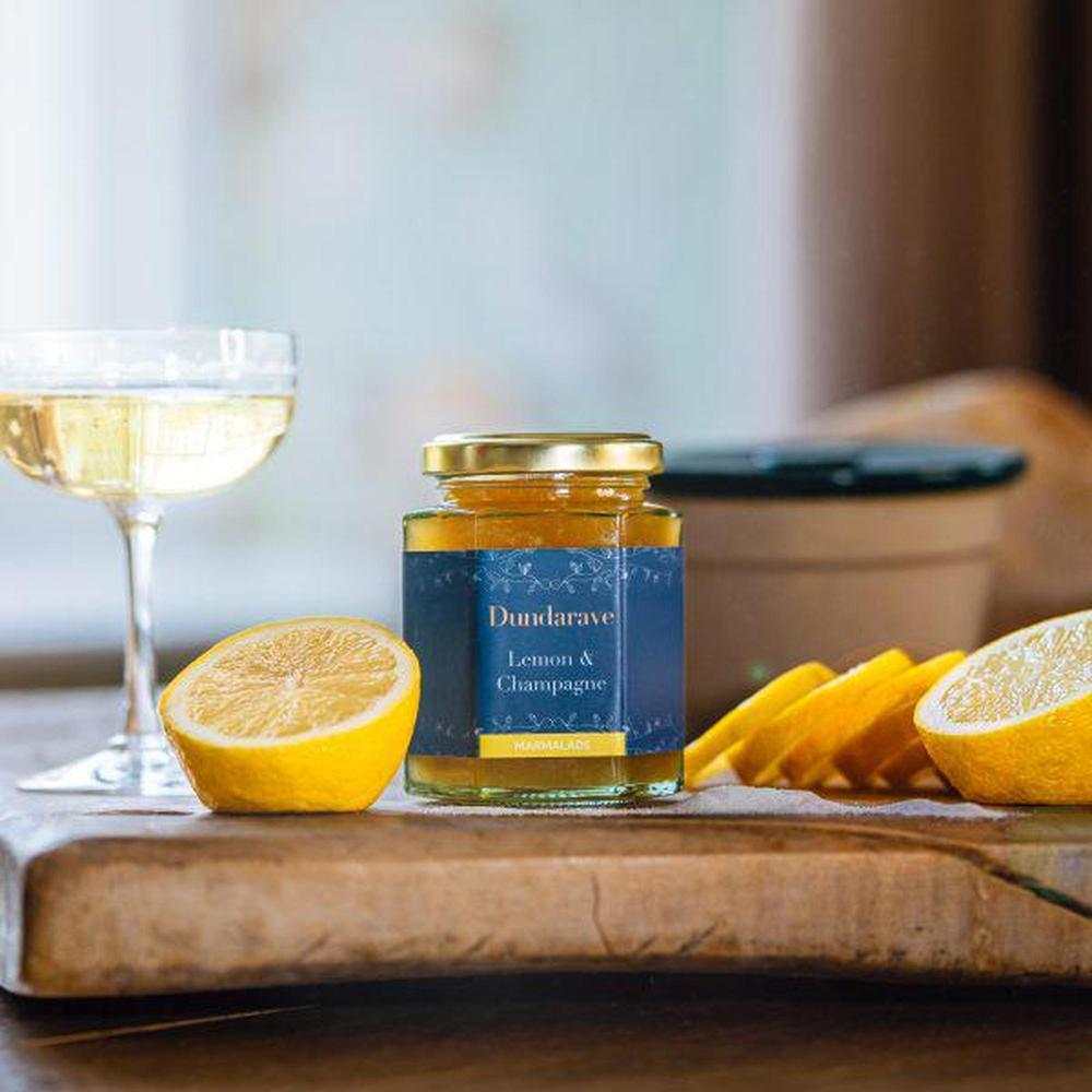 Dundarave Estate Lemon and Champagne marmalade jar with fresh lemons and a glass of champagne on wooden board