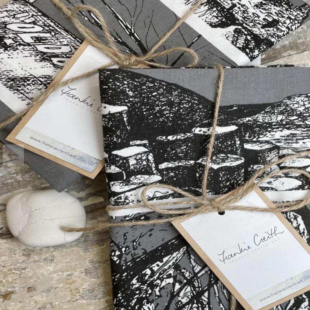 North Coast Tea Towel with black and white pen and ink illustrations of iconic Northern Ireland landmarks, tied with jute string and labeled