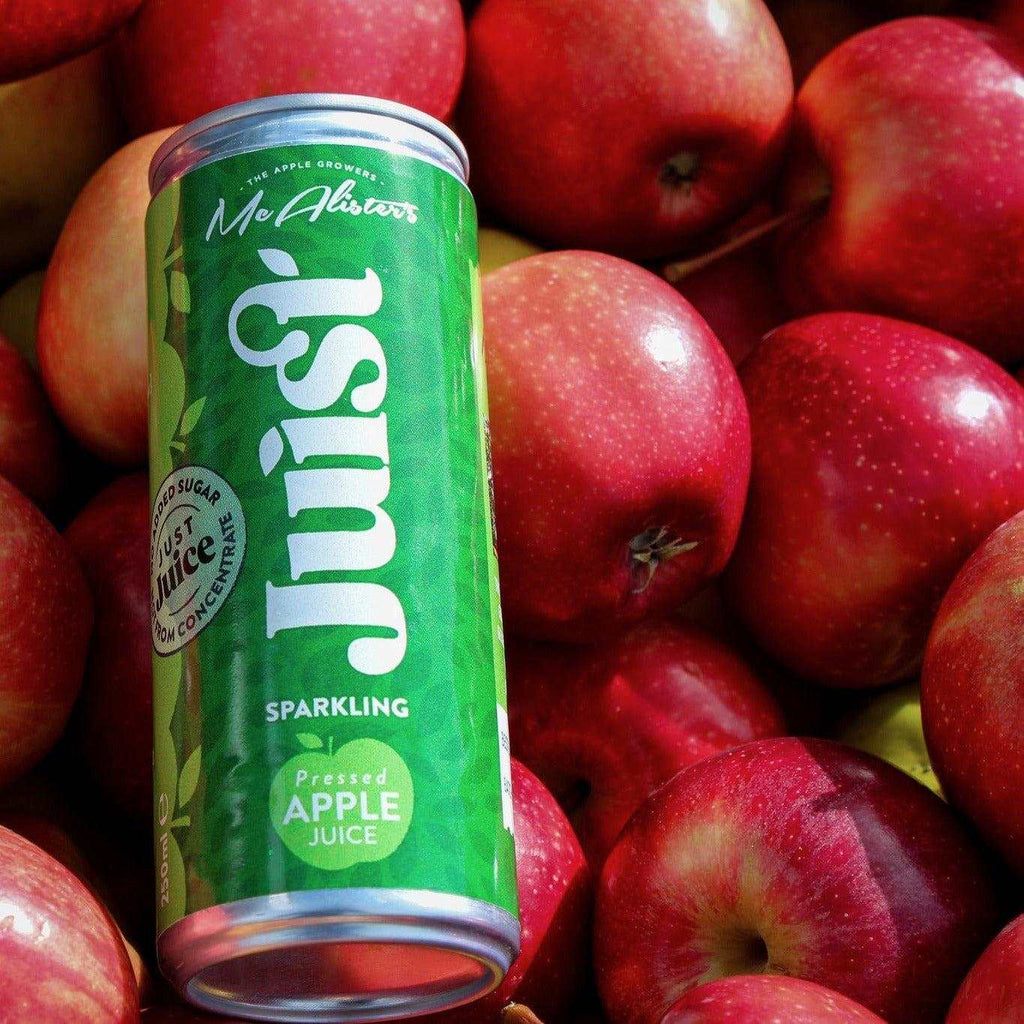 Can of Mc Alisters Juist sparkling apple juice surrounded by fresh red apples