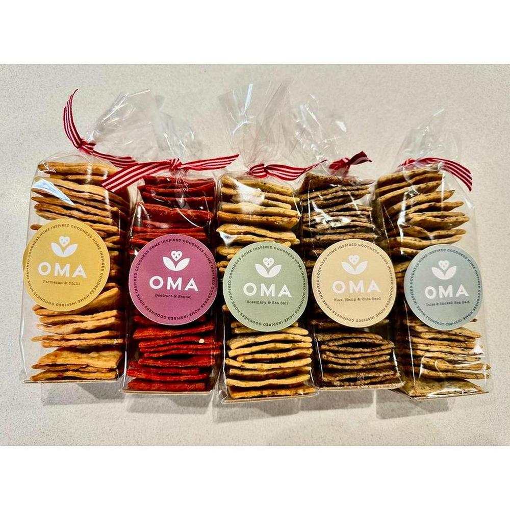 Pack of OMA crackers in various flavors including Parmesan and Chilli, Rosemary and Sea Salt, Beetroot and Fennel, Spinach and Dukkah, Flax Hemp and Chia Seed.
